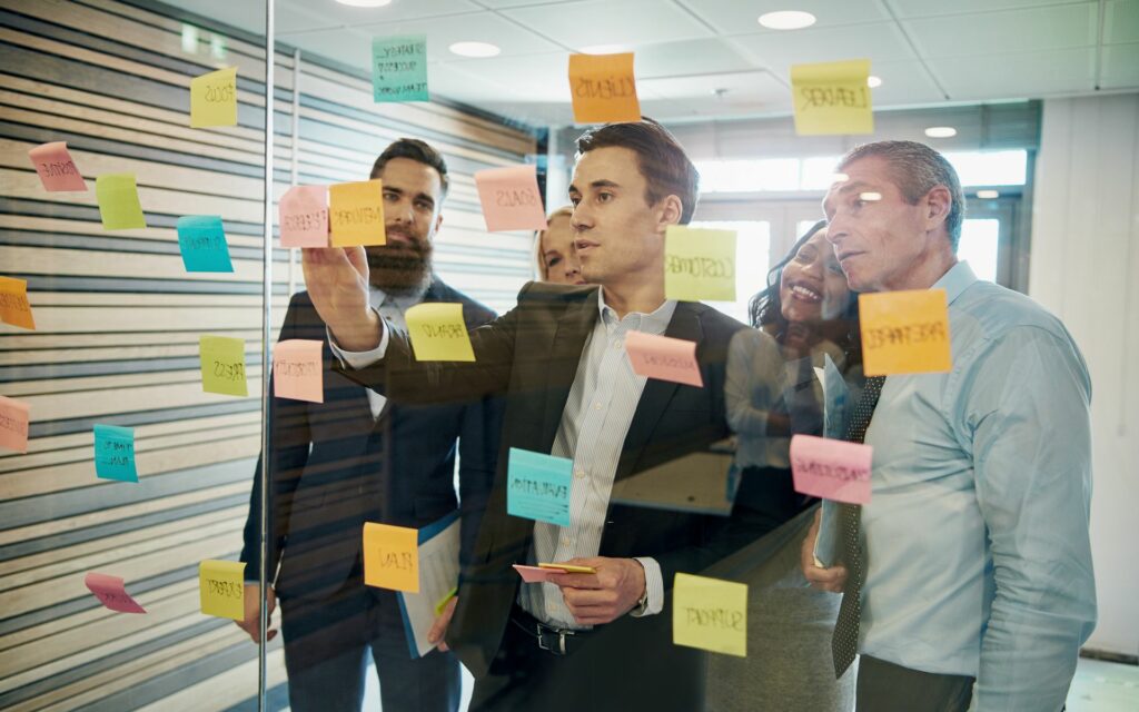 Group,Of,Business,People,Brainstorming,With,Sticky,Notes,On,Glass